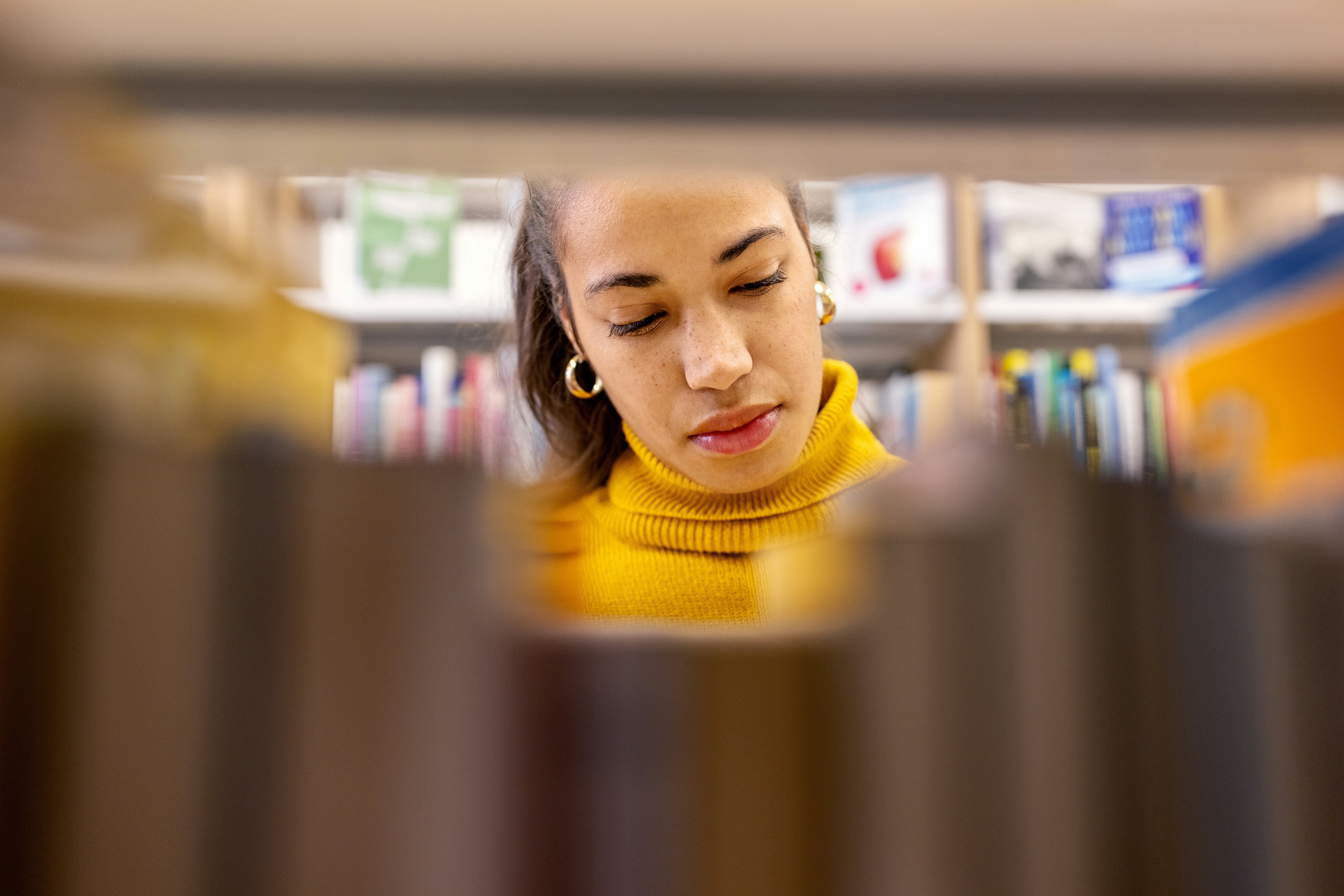 African woman student looking for book at library bookshelf. Young female searching for book on book...