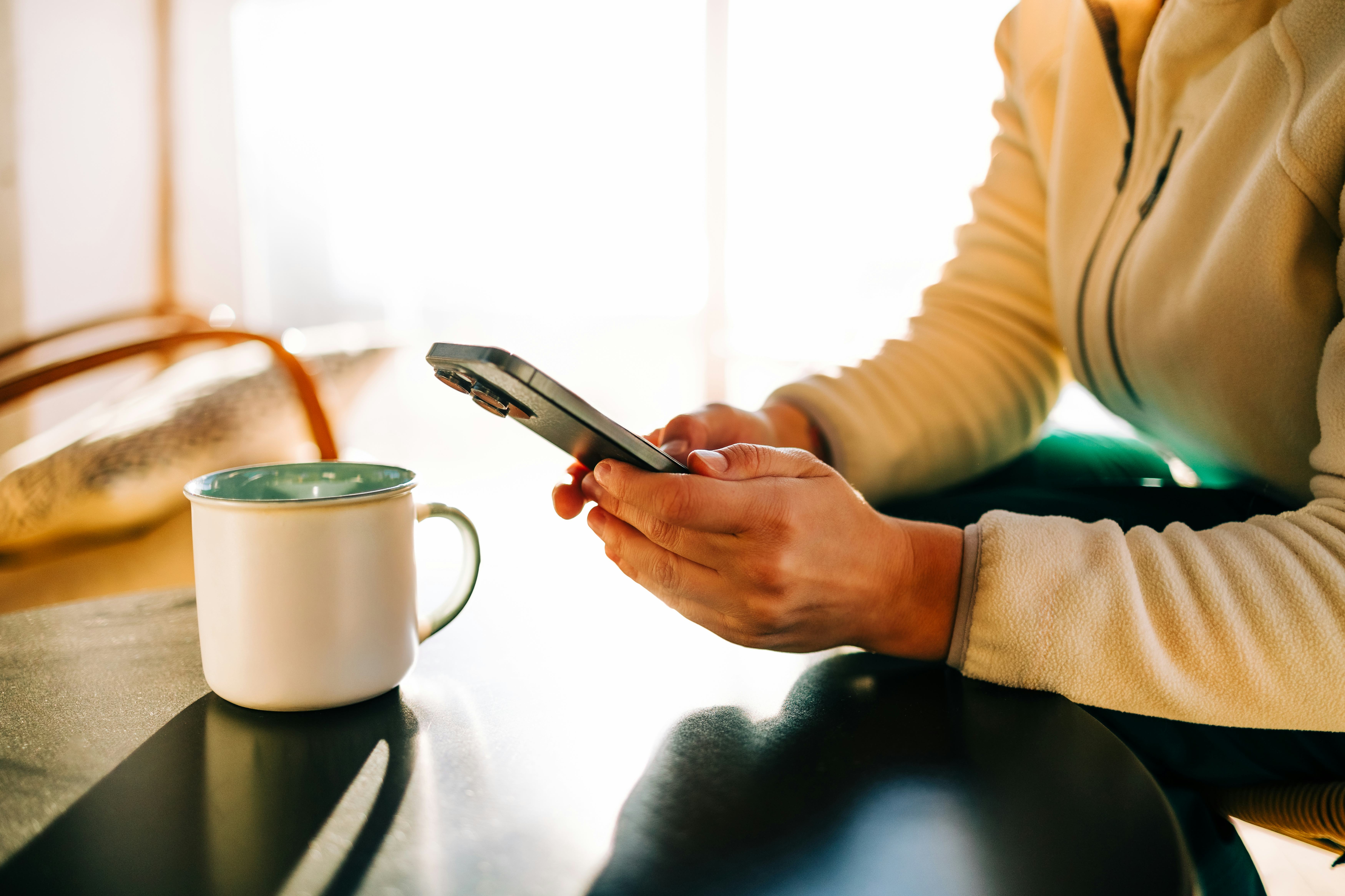 Woman relaxing at home, enjoying a cup of coffee and browsing on her smartphone