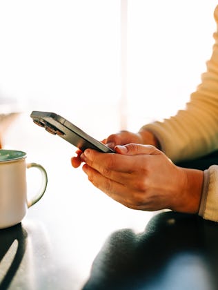 Woman relaxing at home, enjoying a cup of coffee and browsing on her smartphone