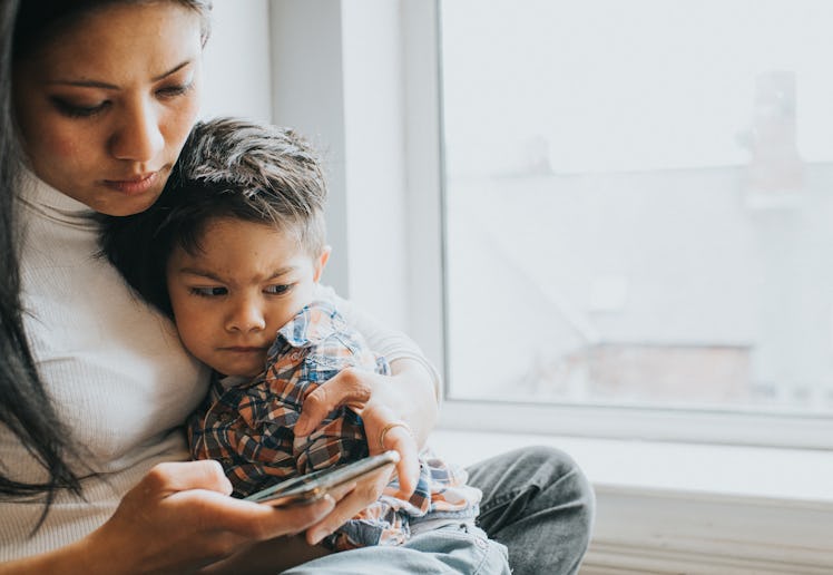 A mother is distracted on a mobile phone as she holds her son close to her. He looks irritated and a...