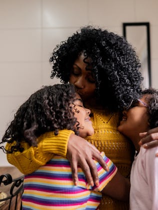 Mother and daughters embracing in the kitchen at home