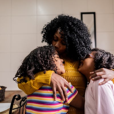 Mother and daughters embracing in the kitchen at home