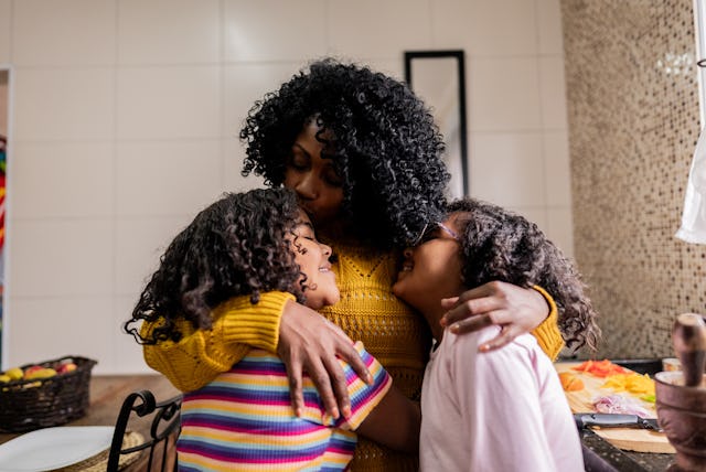 Mother and daughters embracing in the kitchen at home