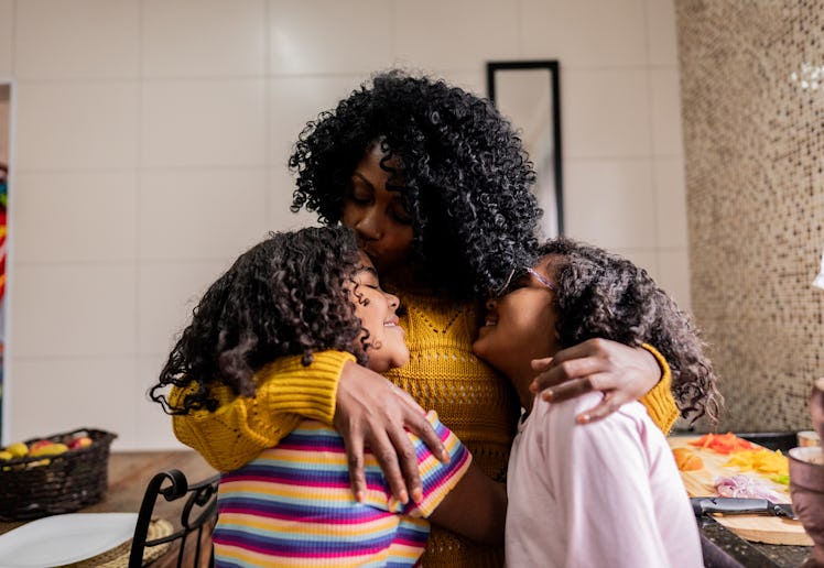 Mother and daughters embracing in the kitchen at home