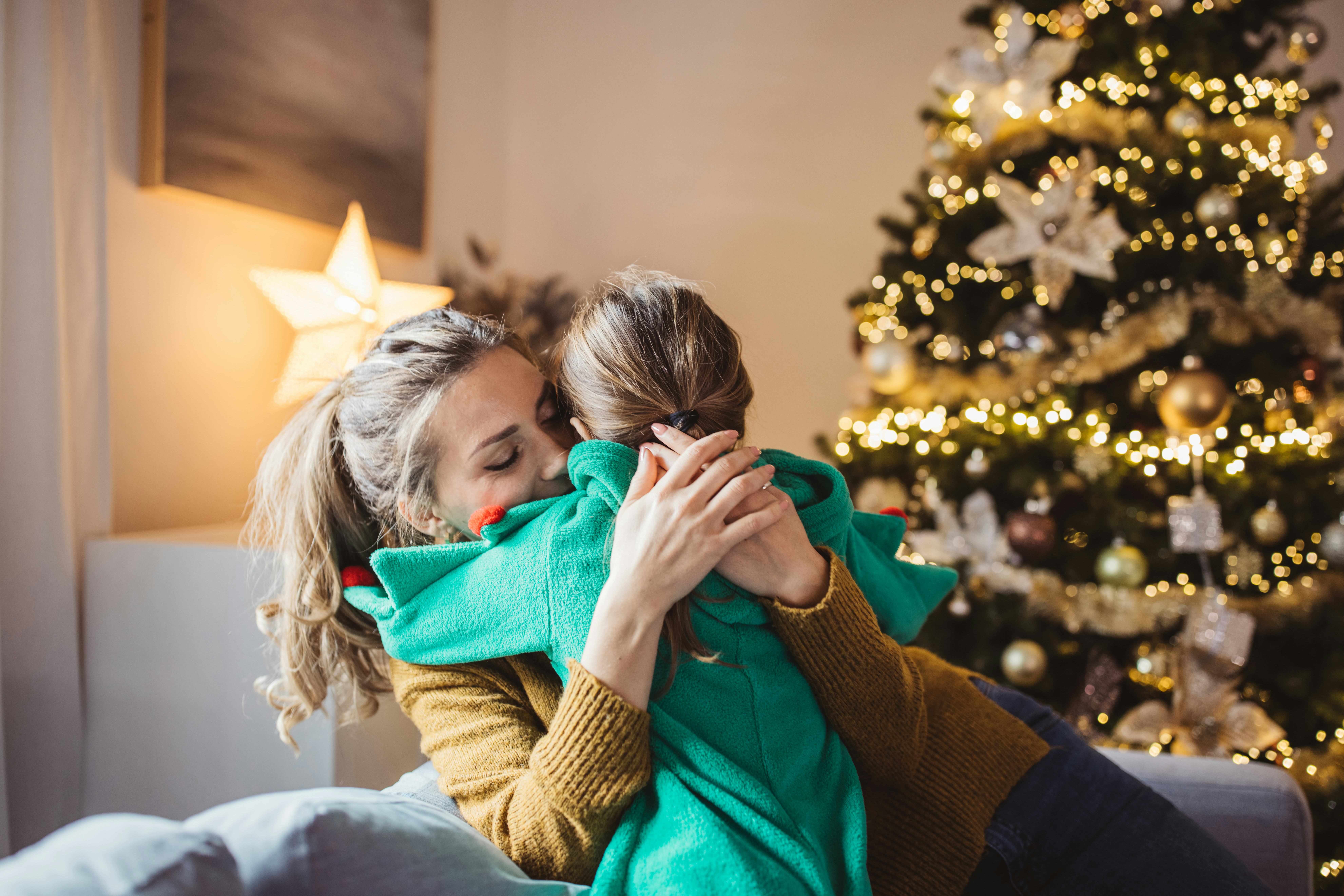 Little girl and her mom on Christmas morning at home. Girl is sad about something and mother is hugg...
