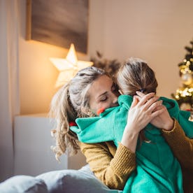 Little girl and her mom on Christmas morning at home. Girl is sad about something and mother is hugg...
