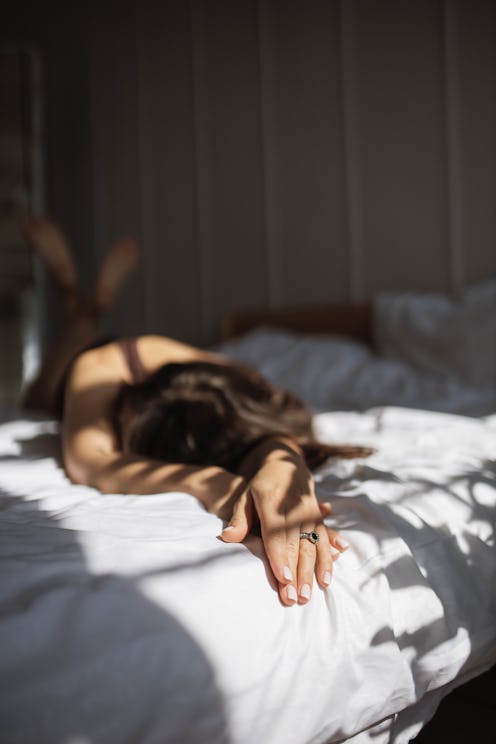 Daydreaming in comfort: Relaxed mature woman with long brown hair lies in cozy bed with white beddin...