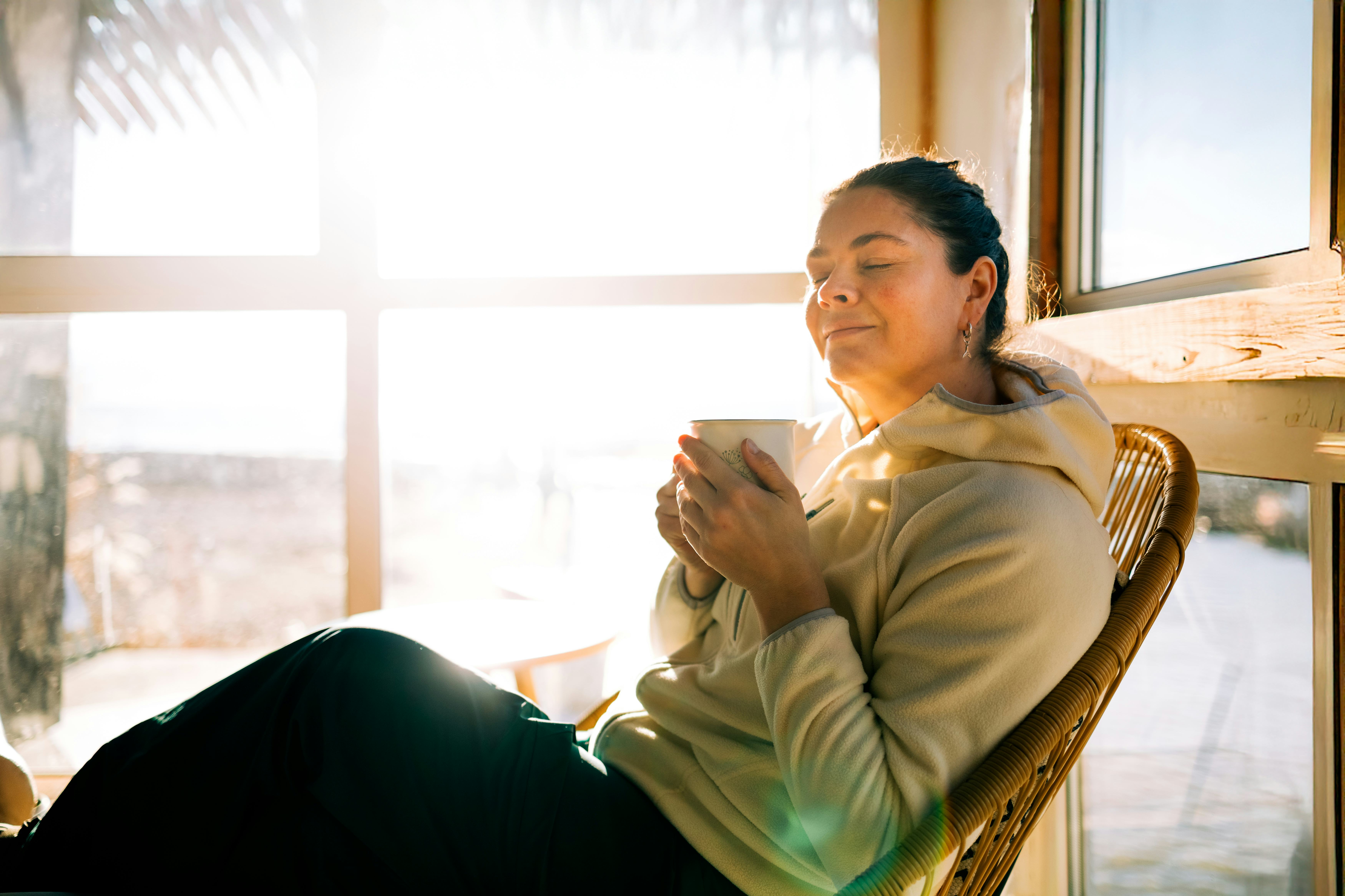 Serene woman relaxing with warm drink by sunny window
