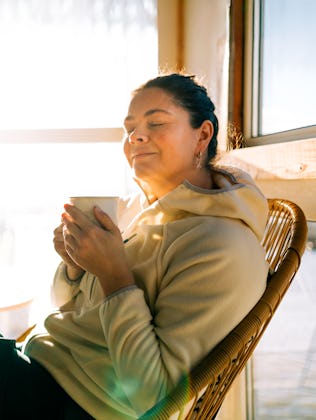 Serene woman relaxing with warm drink by sunny window