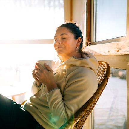 Serene woman relaxing with warm drink by sunny window