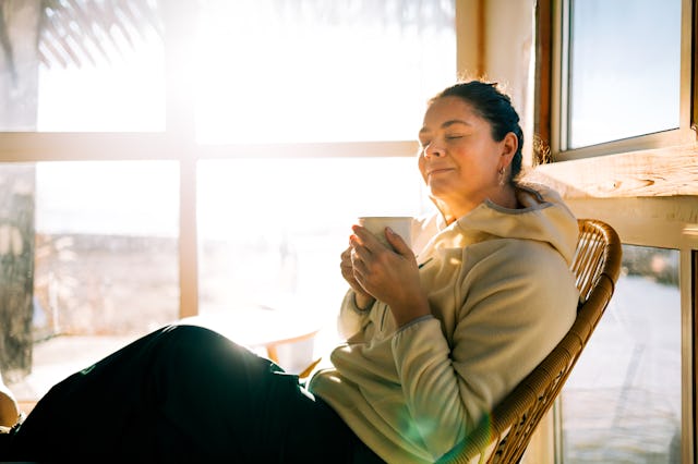 Serene woman relaxing with warm drink by sunny window