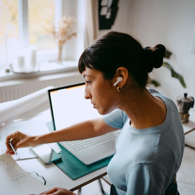 A woman sits at a desk with ear buds in, flipping through a notebook.