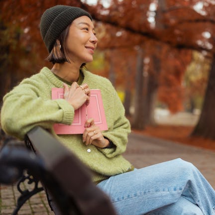 Smiling woman with cap and green sweater holding a book in her hands. She is delighted with the book...