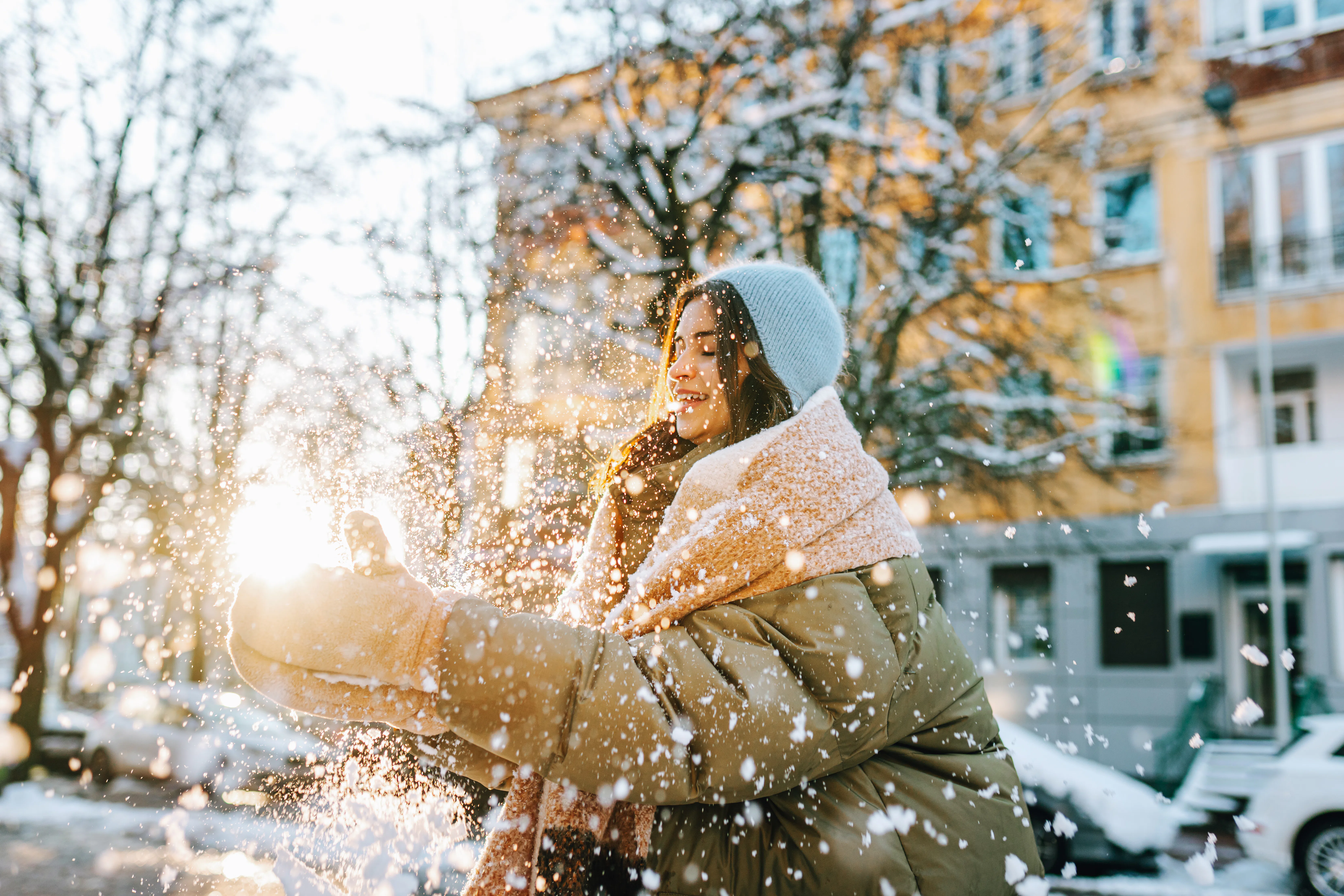 Young woman playing outdoors, throwing fresh snow in bright sun on a cold winter day