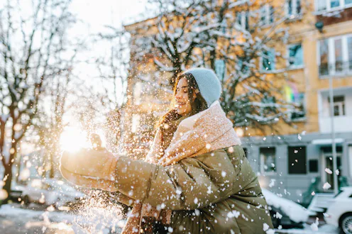Young woman playing outdoors, throwing fresh snow in bright sun on a cold winter day