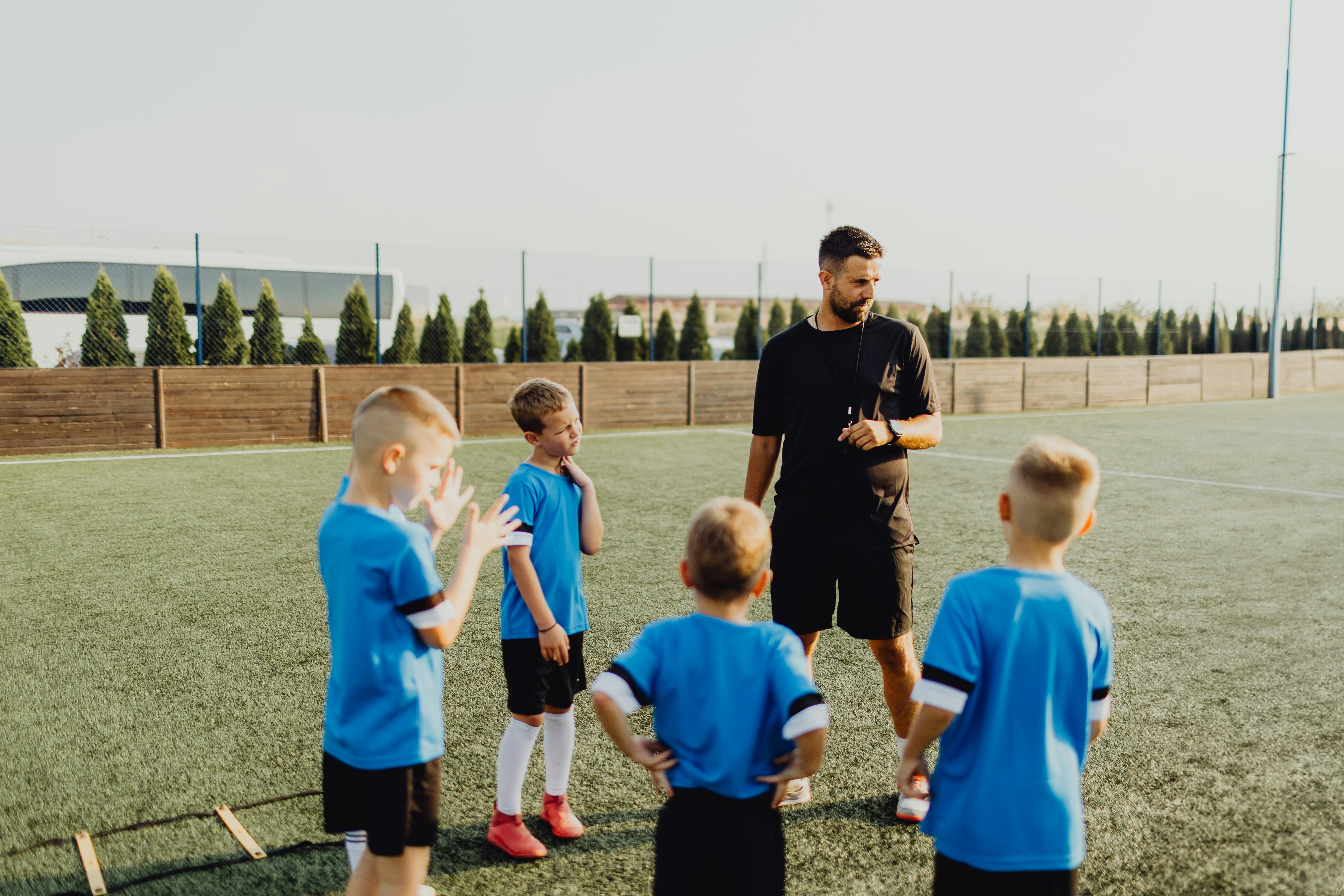 Group of boys standing in front of coach on football field and listening to pre game lecture