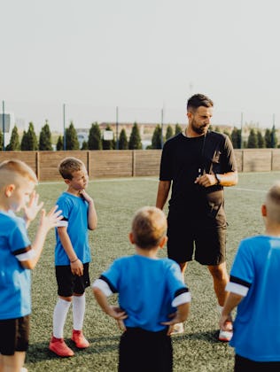 Group of boys standing in front of coach on football field and listening to pre game lecture