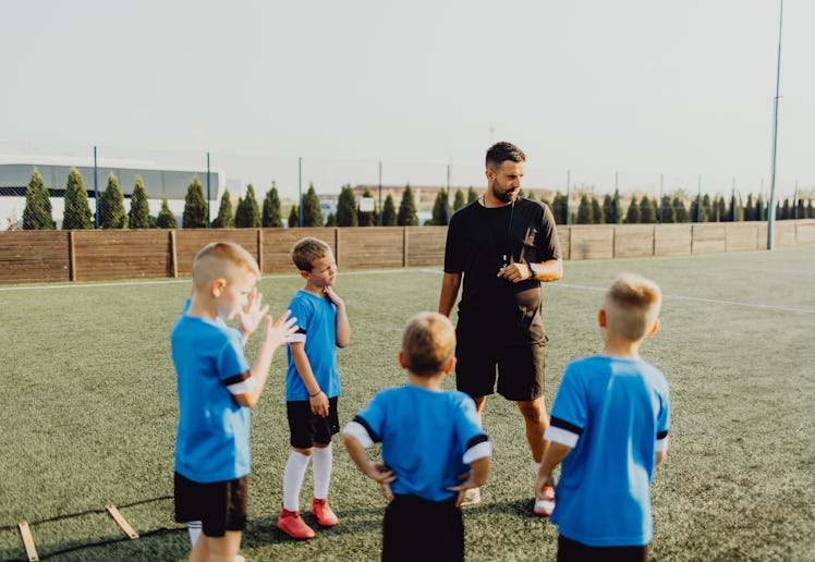 Group of boys standing in front of coach on football field and listening to pre game lecture