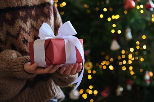 Children's hands are holding a beautiful New Year's gift with a white bow.