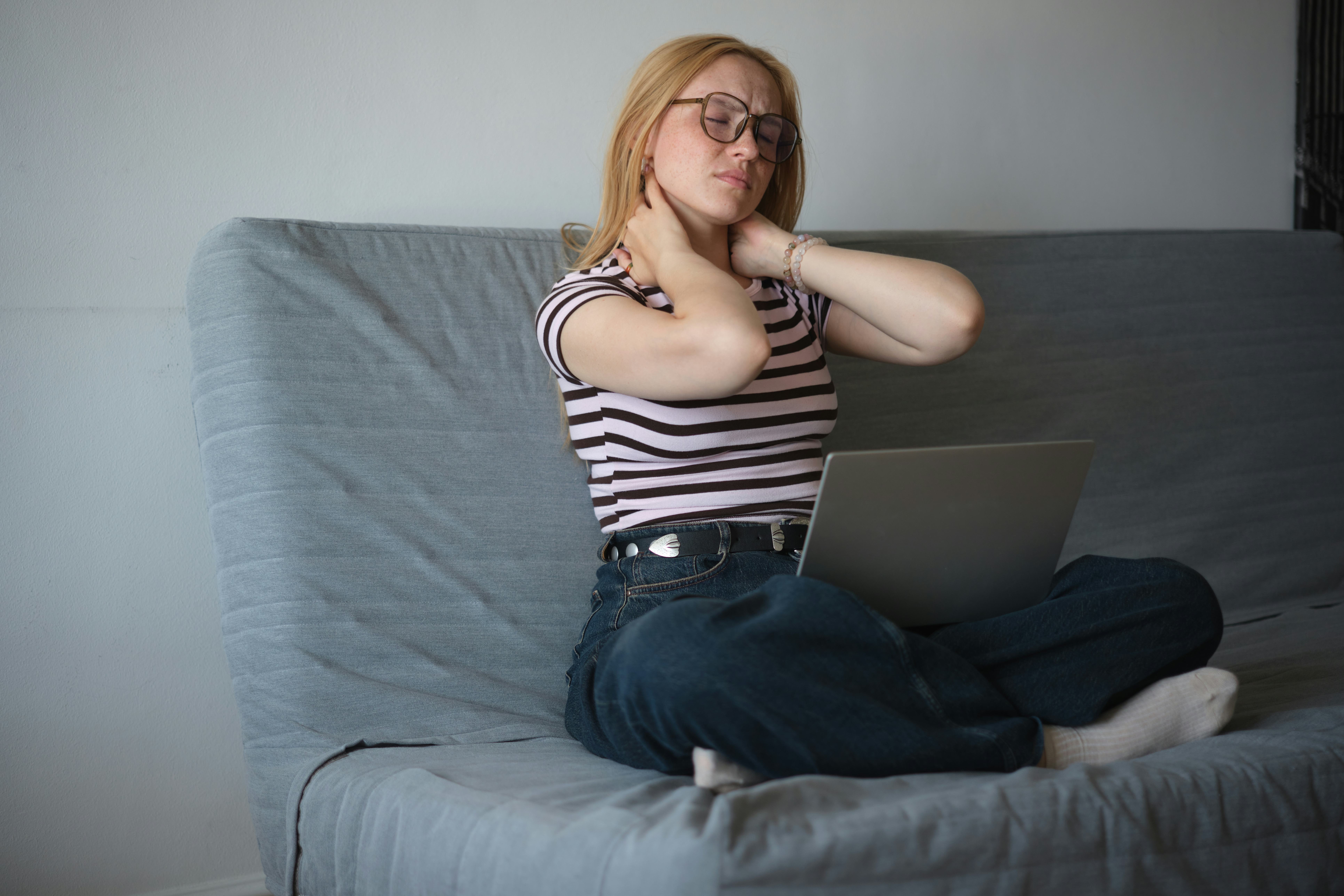 Tired overworked woman freelancer with laptop suffering from neck pain massaging neck while working ...