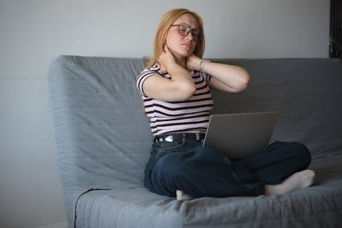 Tired overworked woman freelancer with laptop suffering from neck pain massaging neck while working ...