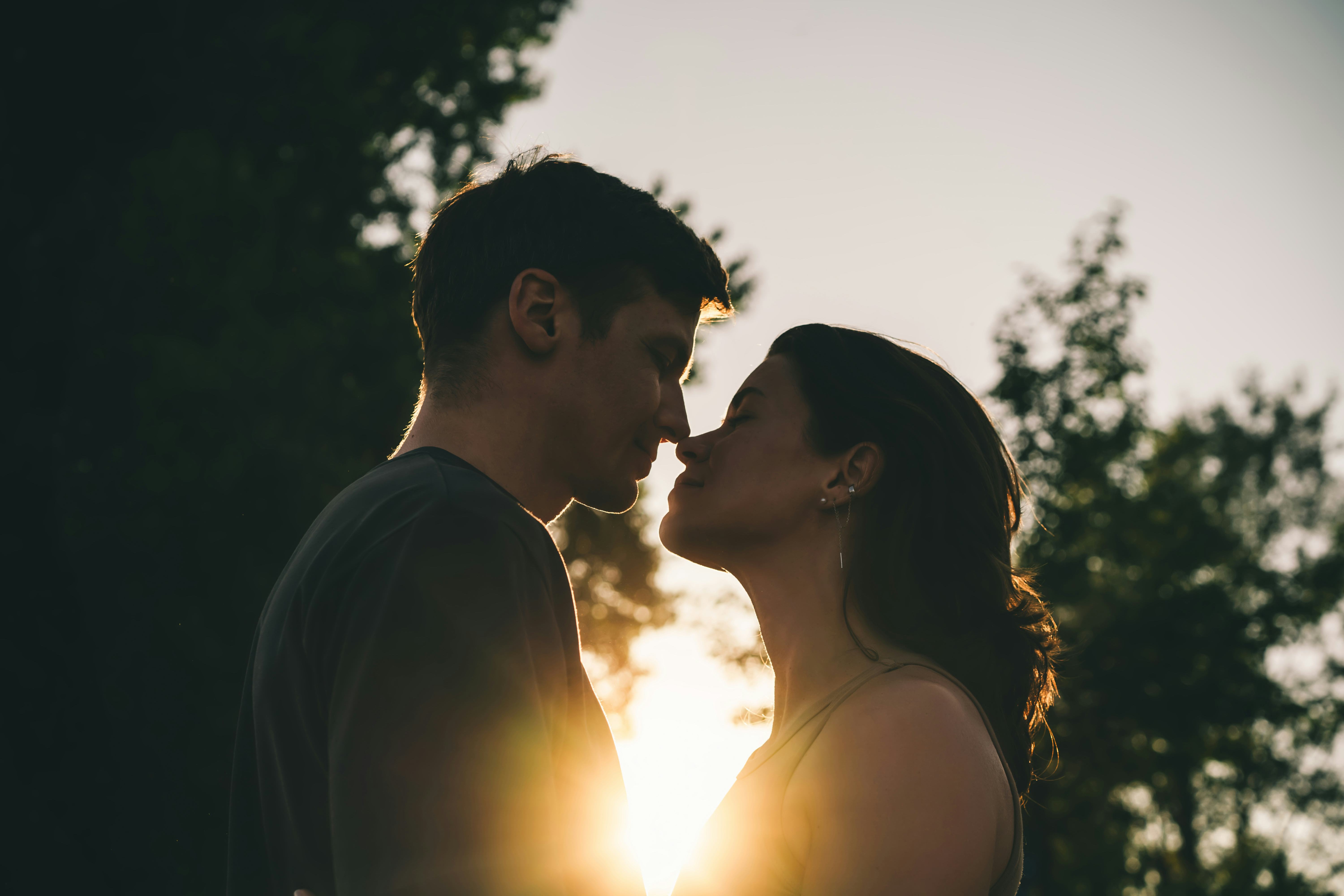 A close-up of a young couple about to kiss with warm sunlight shining between them, highlighting the...