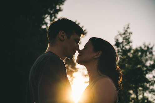 A close-up of a young couple about to kiss with warm sunlight shining between them, highlighting the...