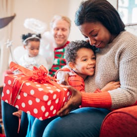A little boy happily hugs his mother as she receives a gift from him on Christmas morning. His siste...