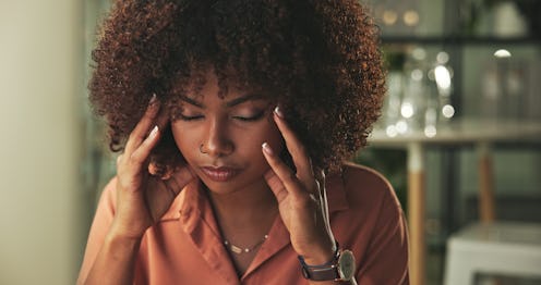 A professional woman appears stressed, holding her temples, amidst a well-lit, modern office space.