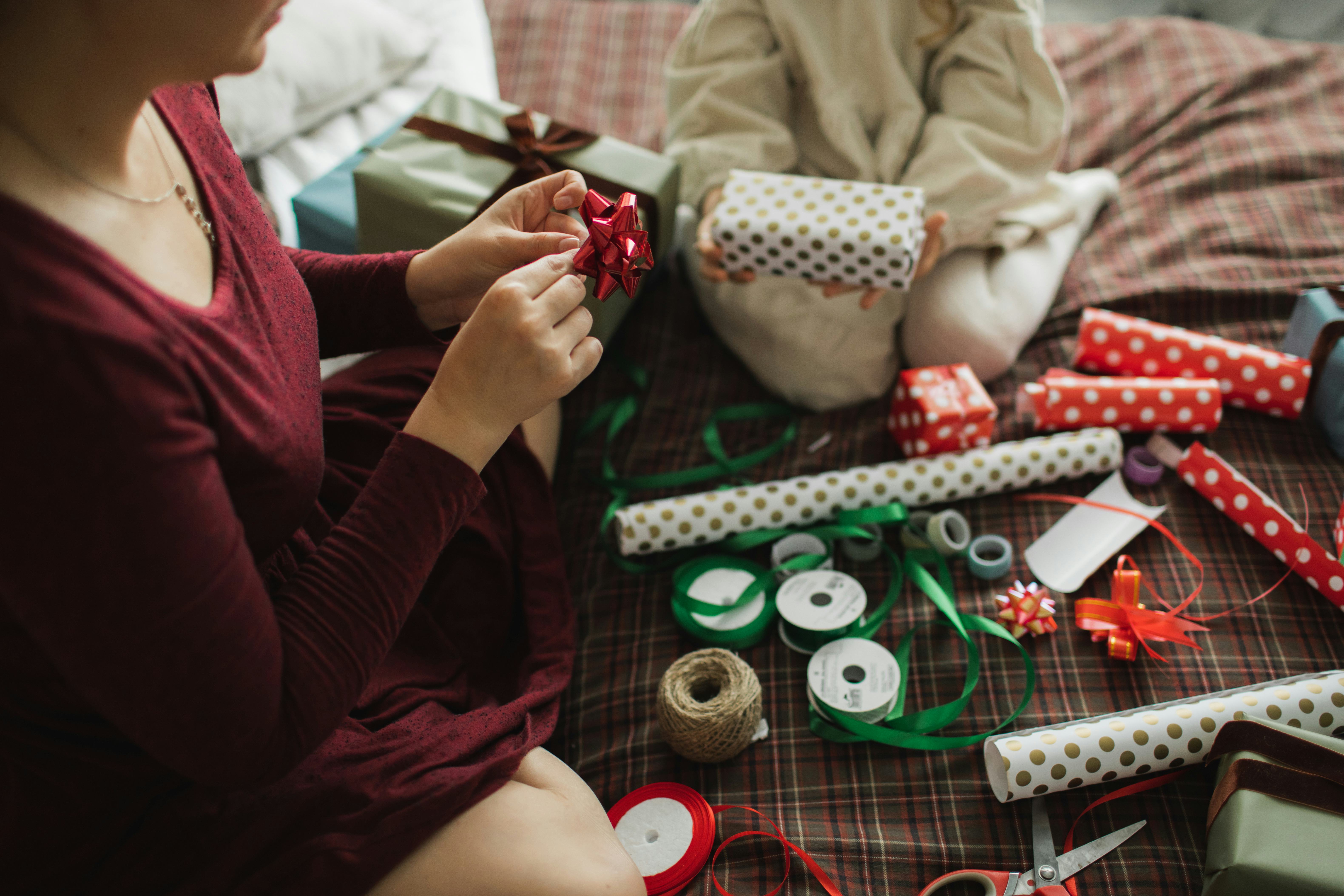 Decorating Christmas gifts, family mother and little girl wrapping Christmas gift box together on be...