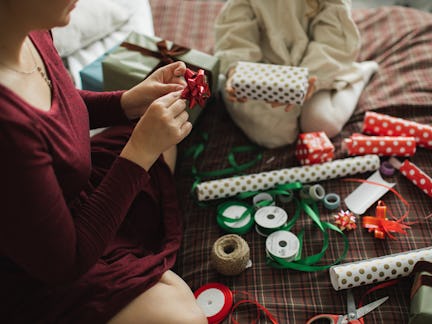 Decorating Christmas gifts, family mother and little girl wrapping Christmas gift box together on be...