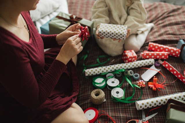 Decorating Christmas gifts, family mother and little girl wrapping Christmas gift box together on be...