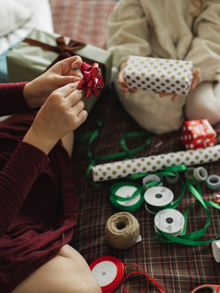 Decorating Christmas gifts, family mother and little girl wrapping Christmas gift box together on be...