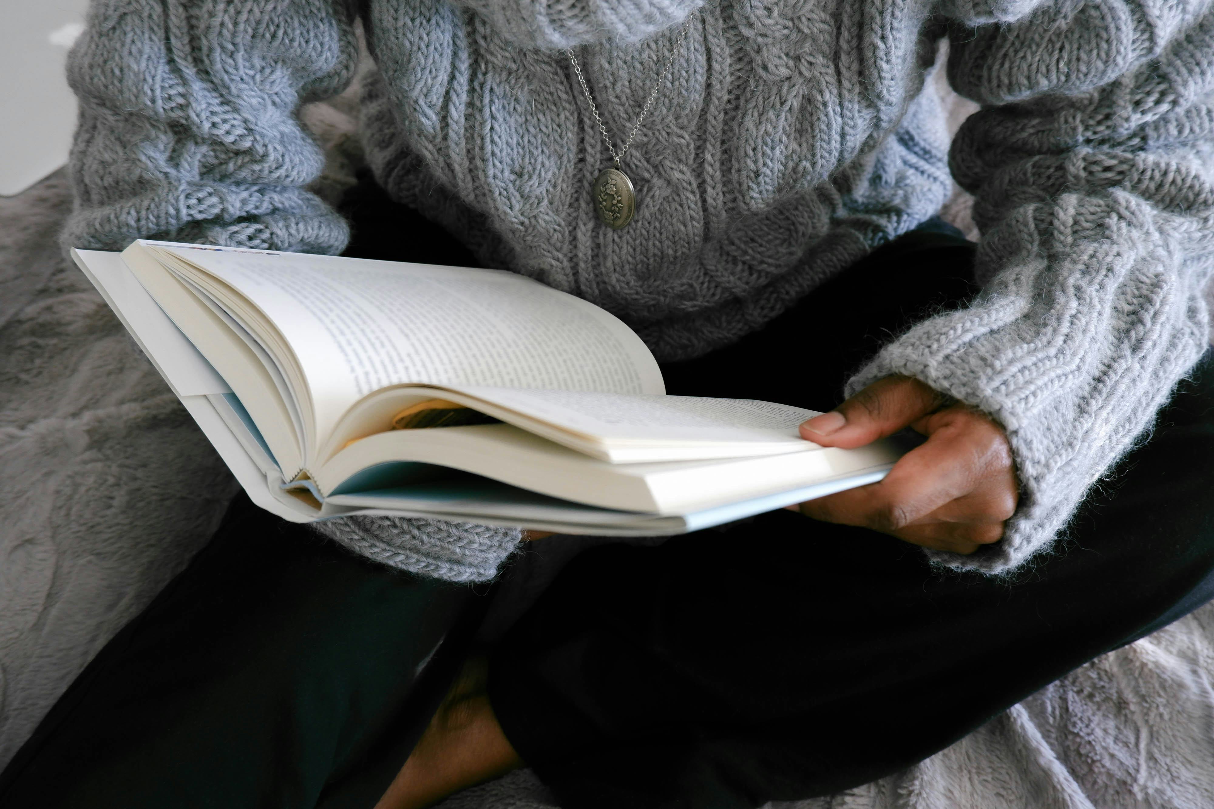 Close-up of unrecognizable black woman lounging in bed reading book