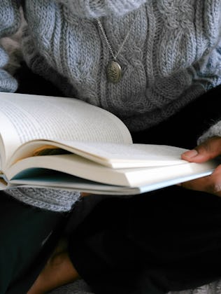 Close-up of unrecognizable black woman lounging in bed reading book