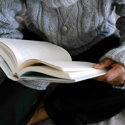 Close-up of unrecognizable black woman lounging in bed reading book
