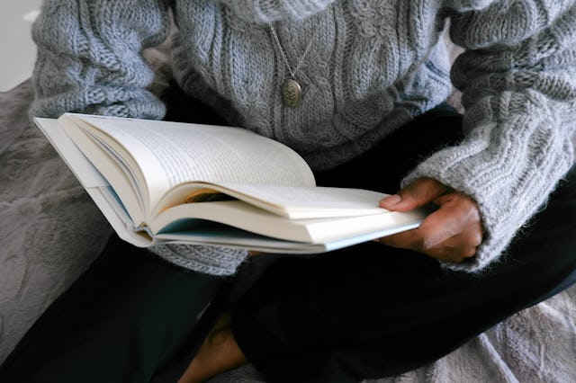 Close-up of unrecognizable black woman lounging in bed reading book