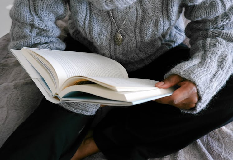 Close-up of unrecognizable black woman lounging in bed reading book
