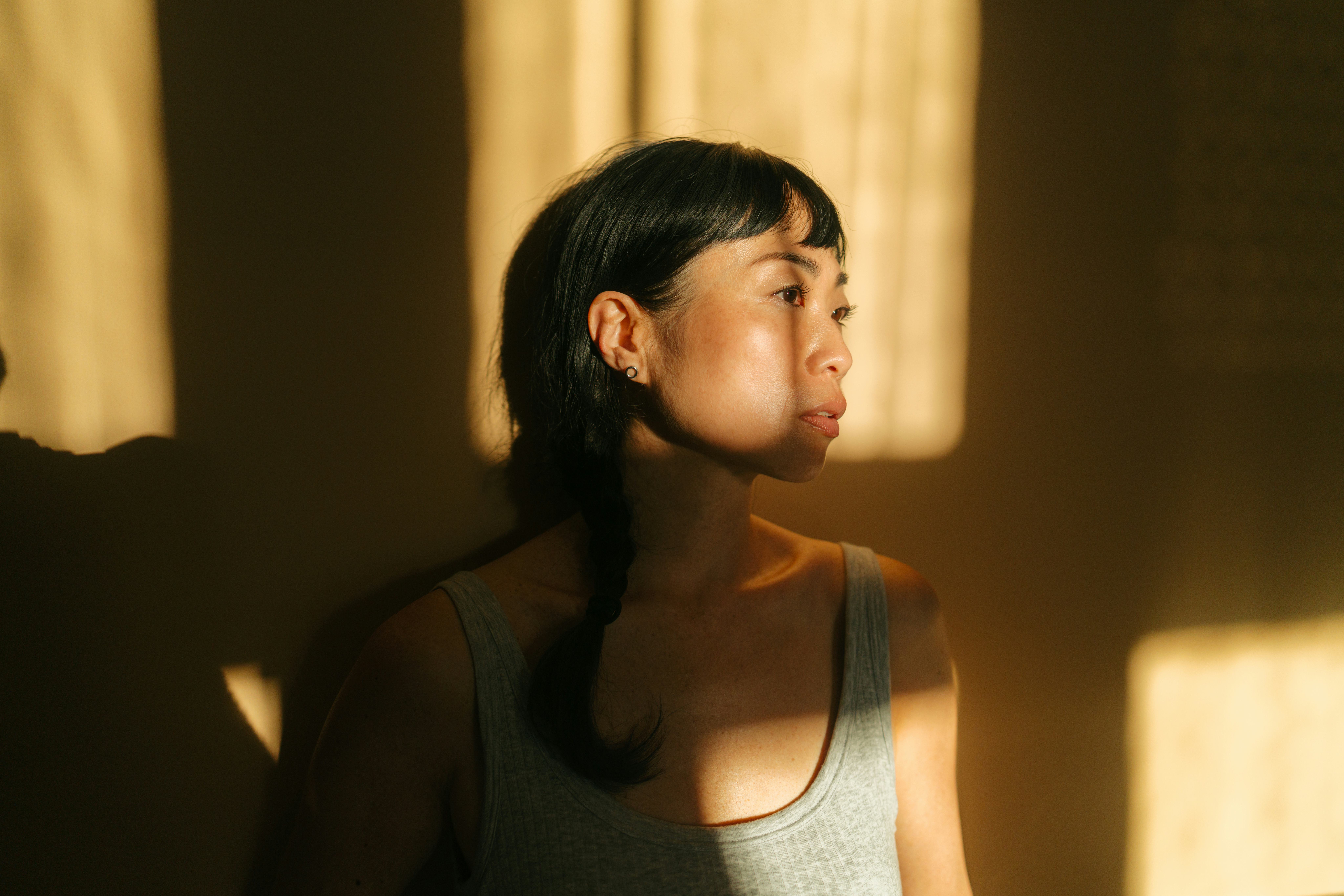 Portrait of a beautiful, mid adult Asian woman, against the orange wall, showered with rays of sun c...