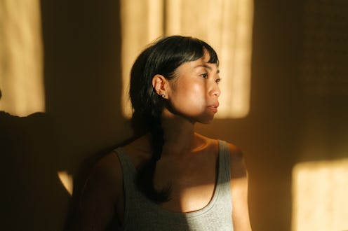Portrait of a beautiful, mid adult Asian woman, against the orange wall, showered with rays of sun c...
