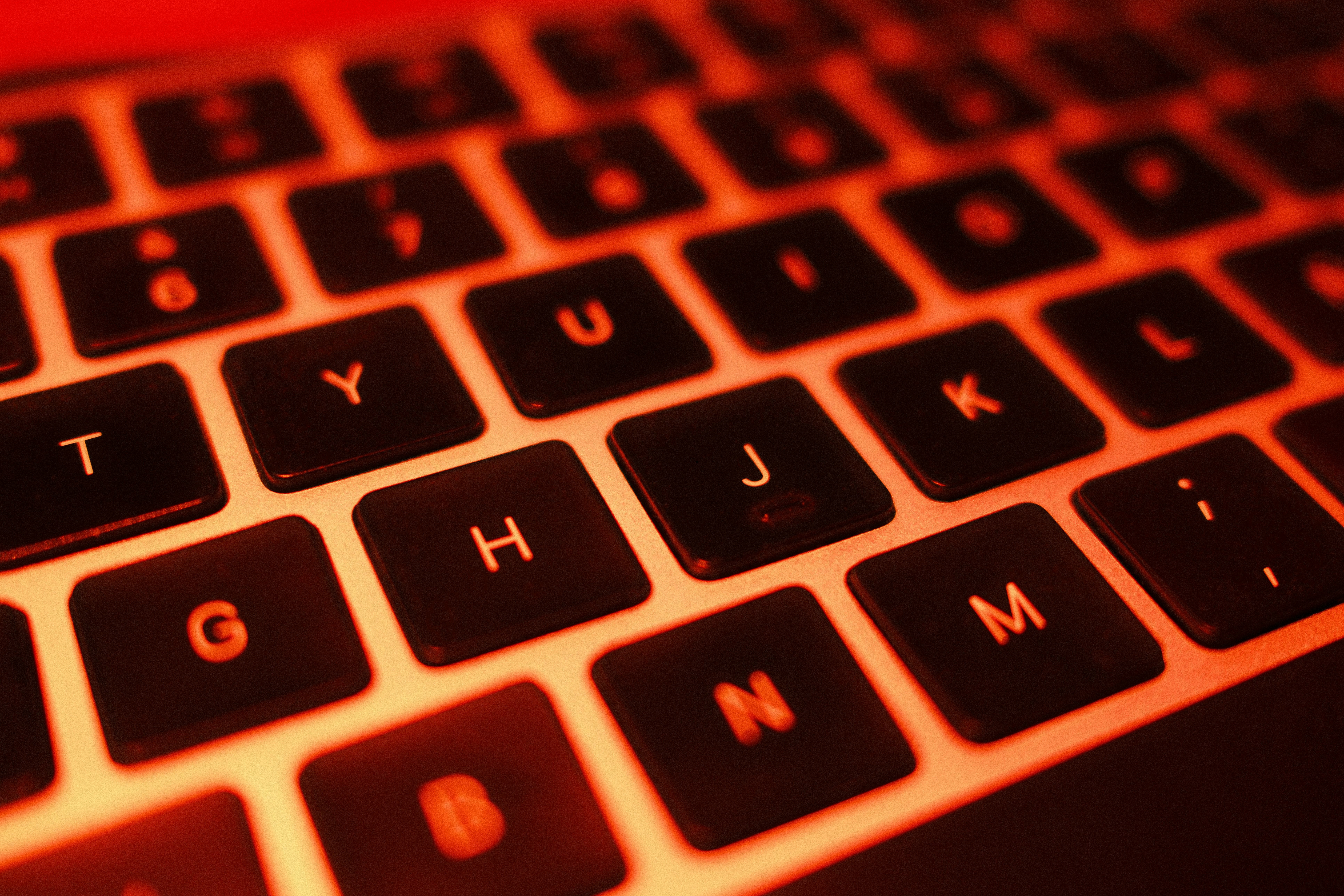 A close-up of a laptop keyboard with intense red lighting, creating a technological and futuristic a...