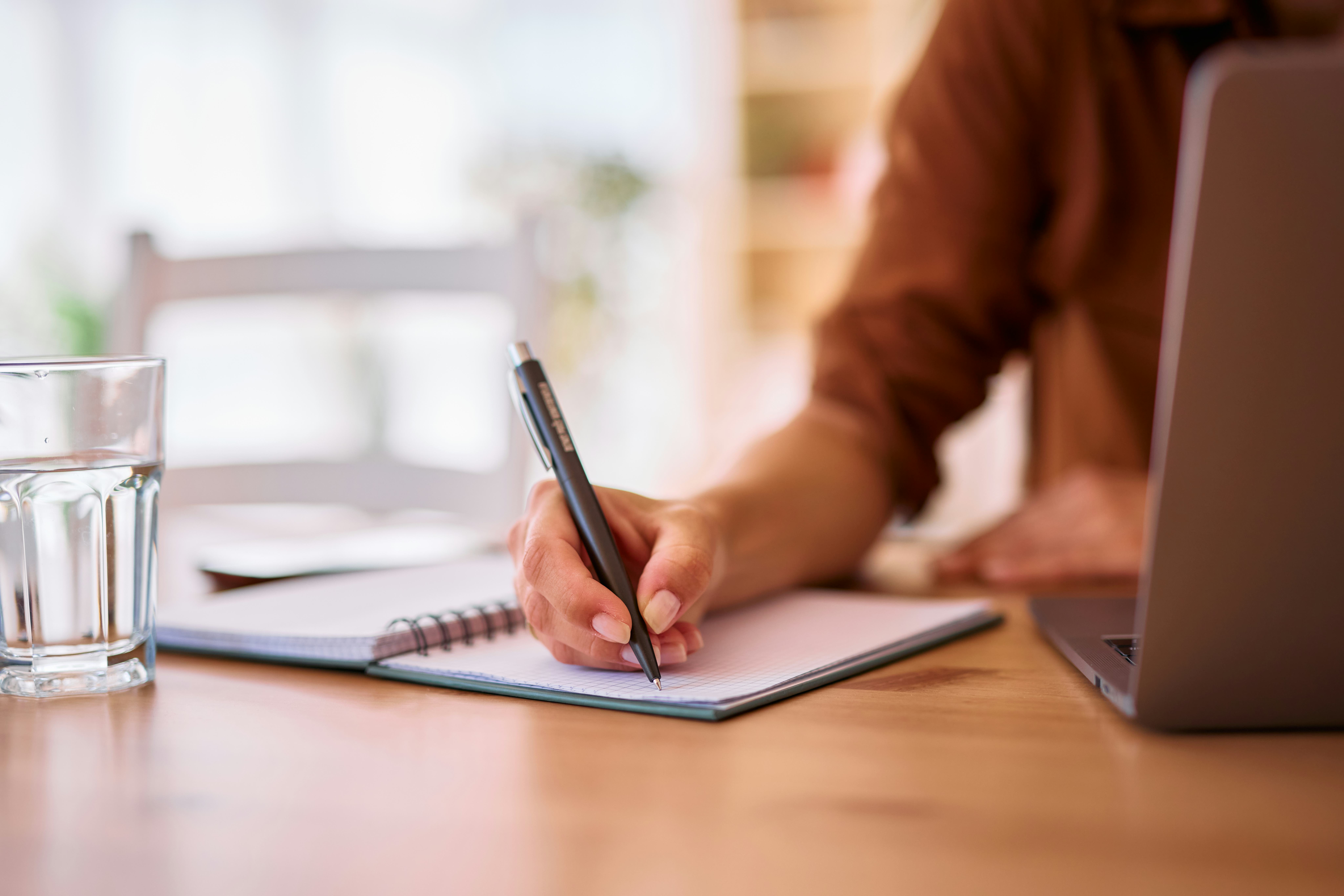 Close-up of female hands writing notes in a notebook while working or studying from home. Utilizing ...
