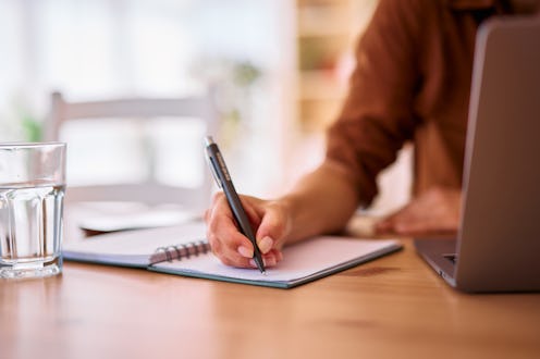 Close-up of female hands writing notes in a notebook while working or studying from home. Utilizing ...