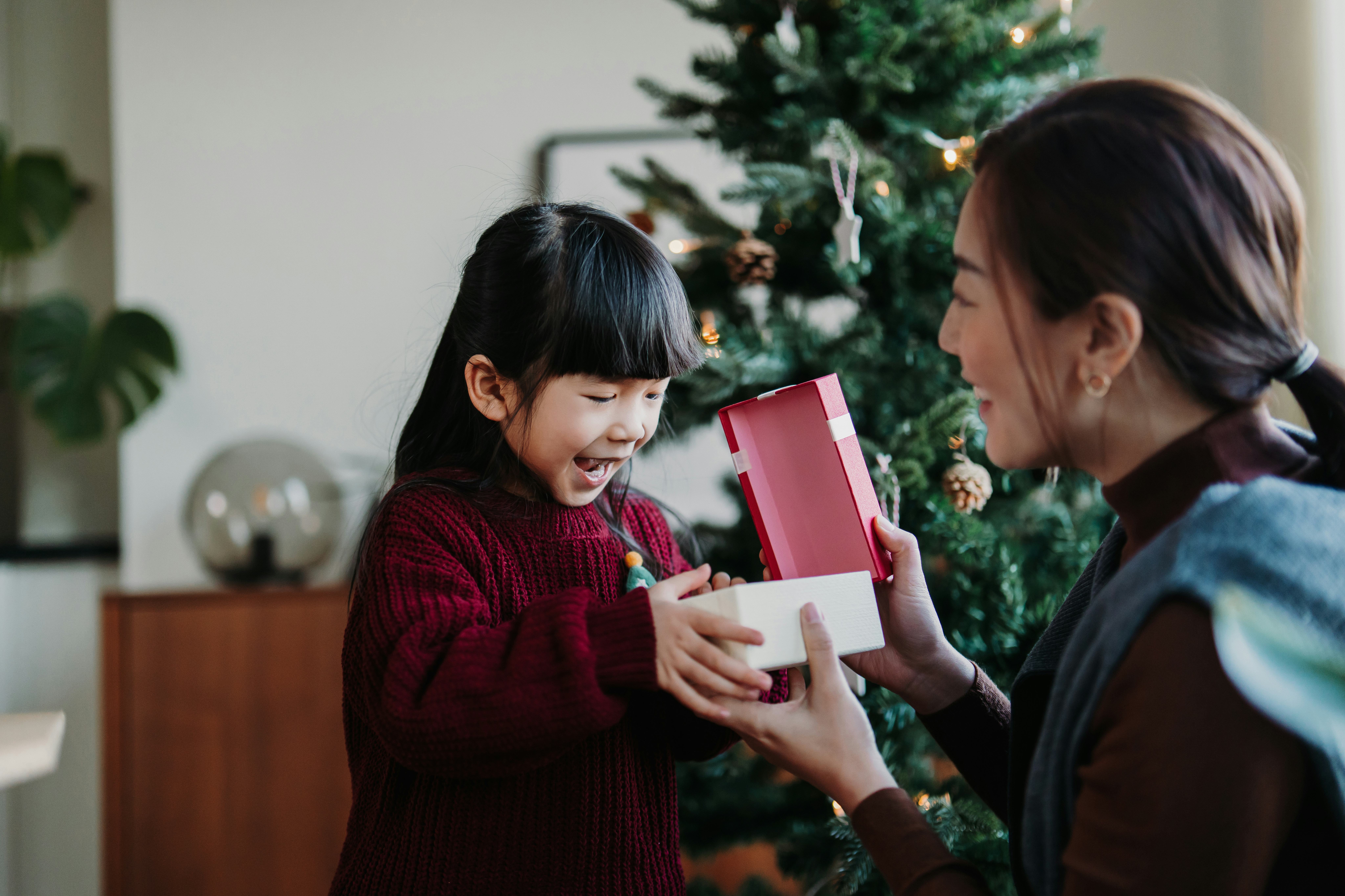 Loving Asian mother and cute little daughter enjoying opening Christmas presents together on Christm...