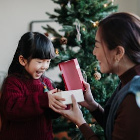 Loving Asian mother and cute little daughter enjoying opening Christmas presents together on Christm...