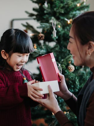 Loving Asian mother and cute little daughter enjoying opening Christmas presents together on Christm...