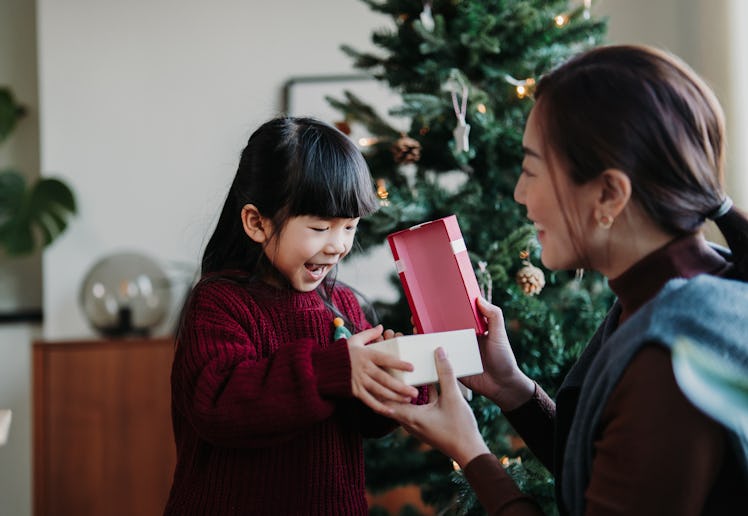 Loving Asian mother and cute little daughter enjoying opening Christmas presents together on Christm...