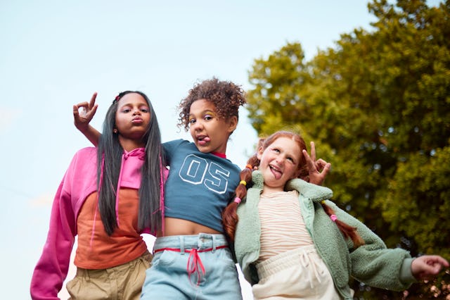 Low angle shot of three young girls striking fun poses outdoors. Vibrant clothing, making faces, pea...