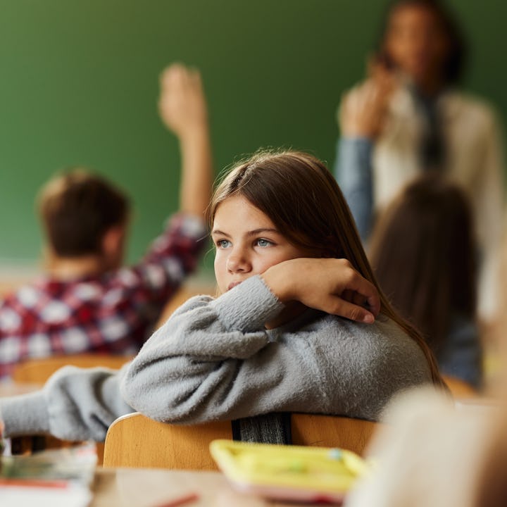 Sad schoolgirl attending a class with her classmates at elementary school.