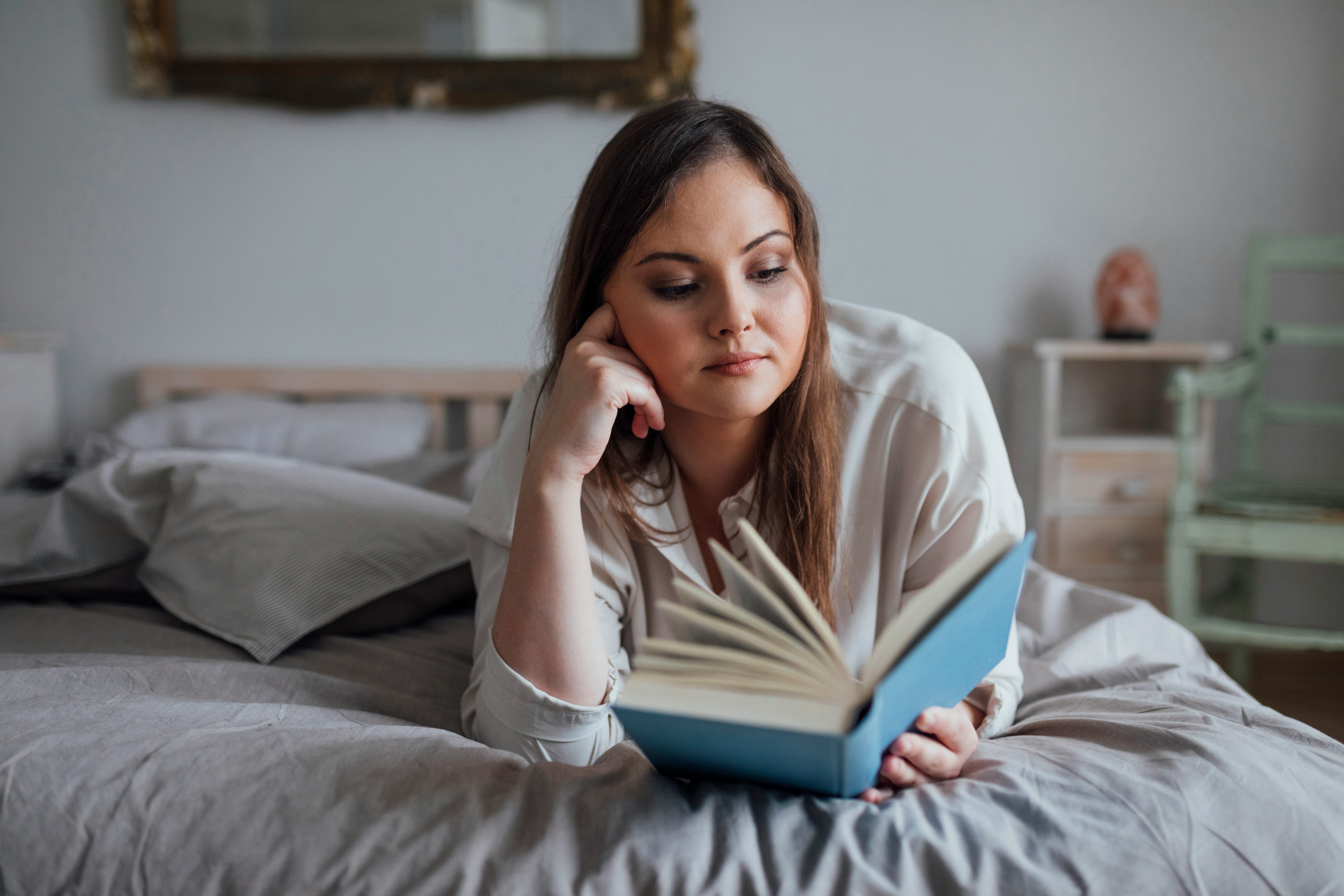 Beautiful young plus size woman lying on her bed and reading a book.